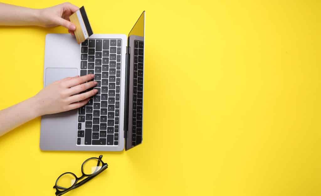 Online payment. Woman with laptop, credit card and glasses on yellow background