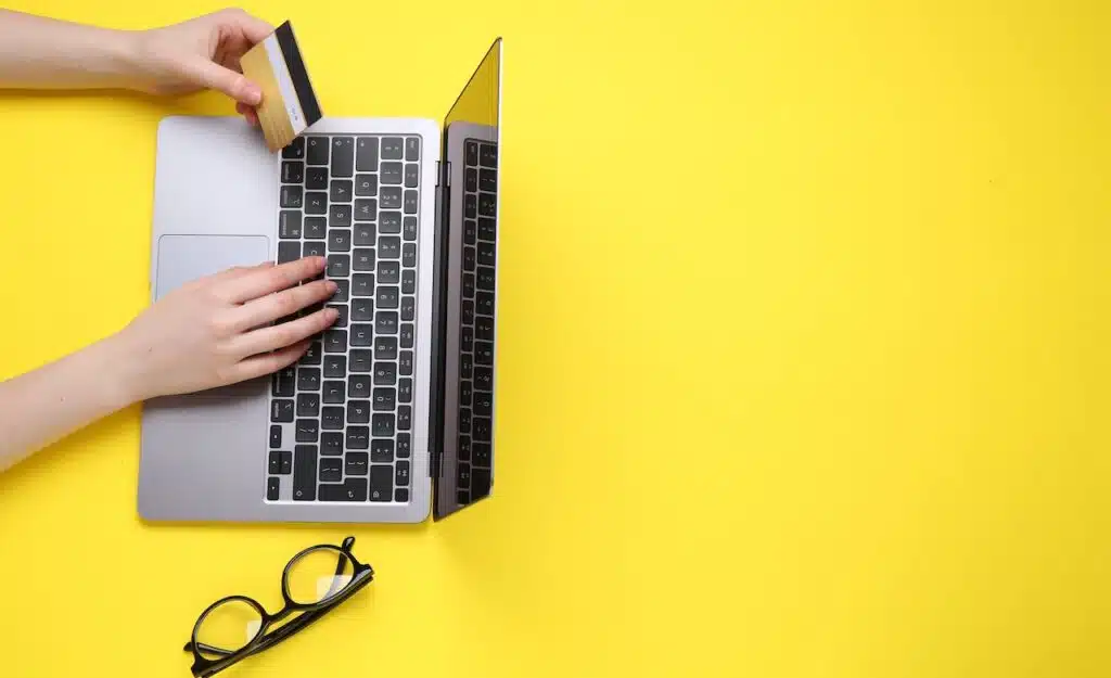 Online payment. Woman with laptop, credit card and glasses on yellow background