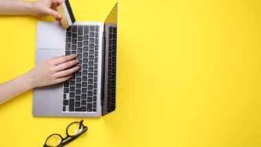 Online payment. Woman with laptop, credit card and glasses on yellow background