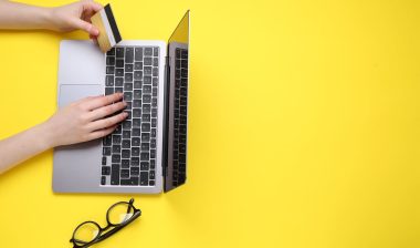 Online payment. Woman with laptop, credit card and glasses on yellow background