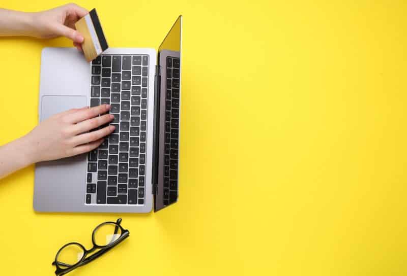 Online payment. Woman with laptop, credit card and glasses on yellow background