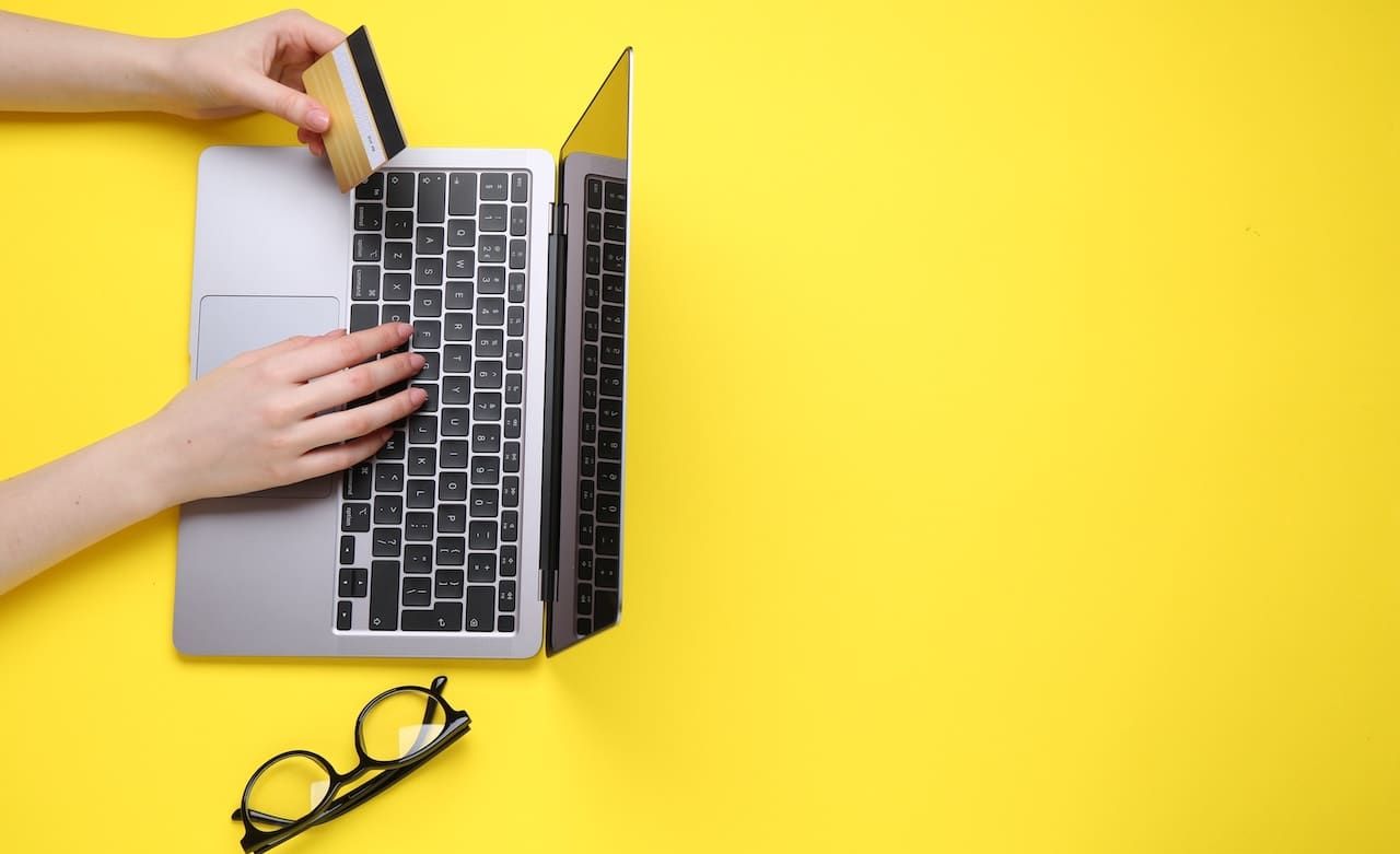 Online payment. Woman with laptop, credit card and glasses on yellow background