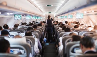 nterior of airplane with passengers on seats and stewardess in uniform