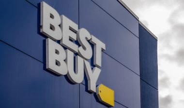 The exterior of a Best Buy store featuring the prominent white "BEST BUY" lettering and yellow tag logo against a dark blue facade.