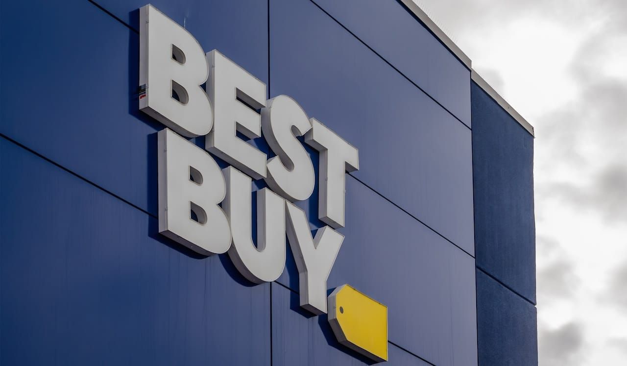 The exterior of a Best Buy store featuring the prominent white "BEST BUY" lettering and yellow tag logo against a dark blue facade.