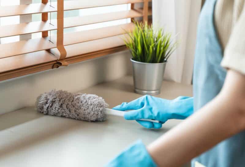 housemaid cleaning furniture surface with sanitizer spray and wiping with wet cloth in living room