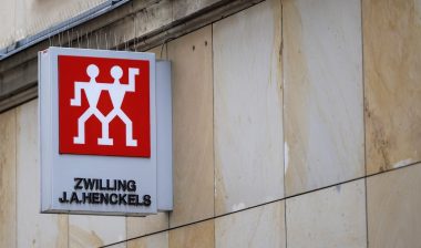Zwilling J.A. Henckels storefront sign with the red twin figures logo is mounted on a stone building facade in an urban setting.