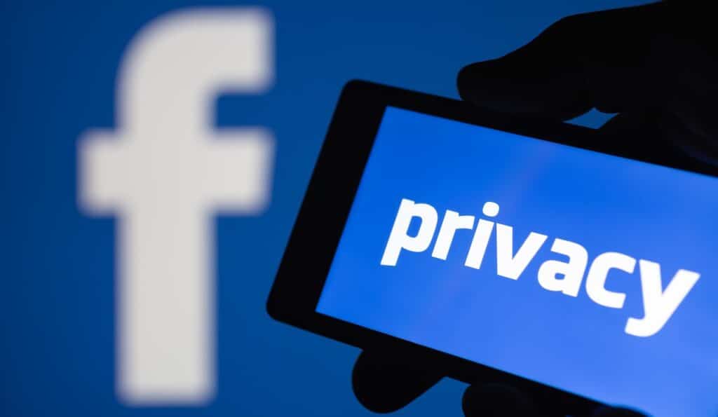 A smartphone in hand displaying the privacy text. Logo of the Facebook blurred on background.