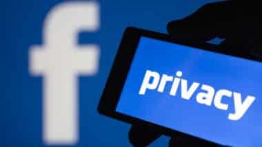 A smartphone in hand displaying the privacy text. Logo of the Facebook blurred on background.
