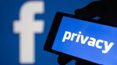 A smartphone in hand displaying the privacy text. Logo of the Facebook blurred on background.