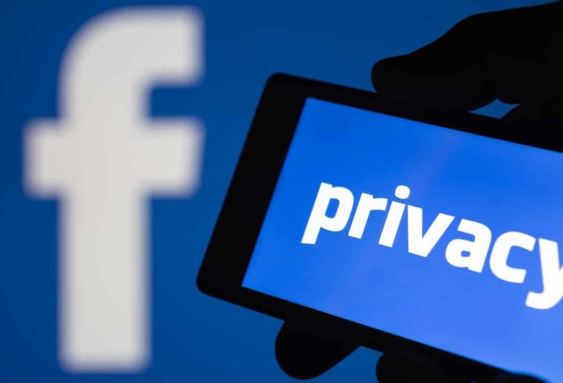 A smartphone in hand displaying the privacy text. Logo of the Facebook blurred on background.