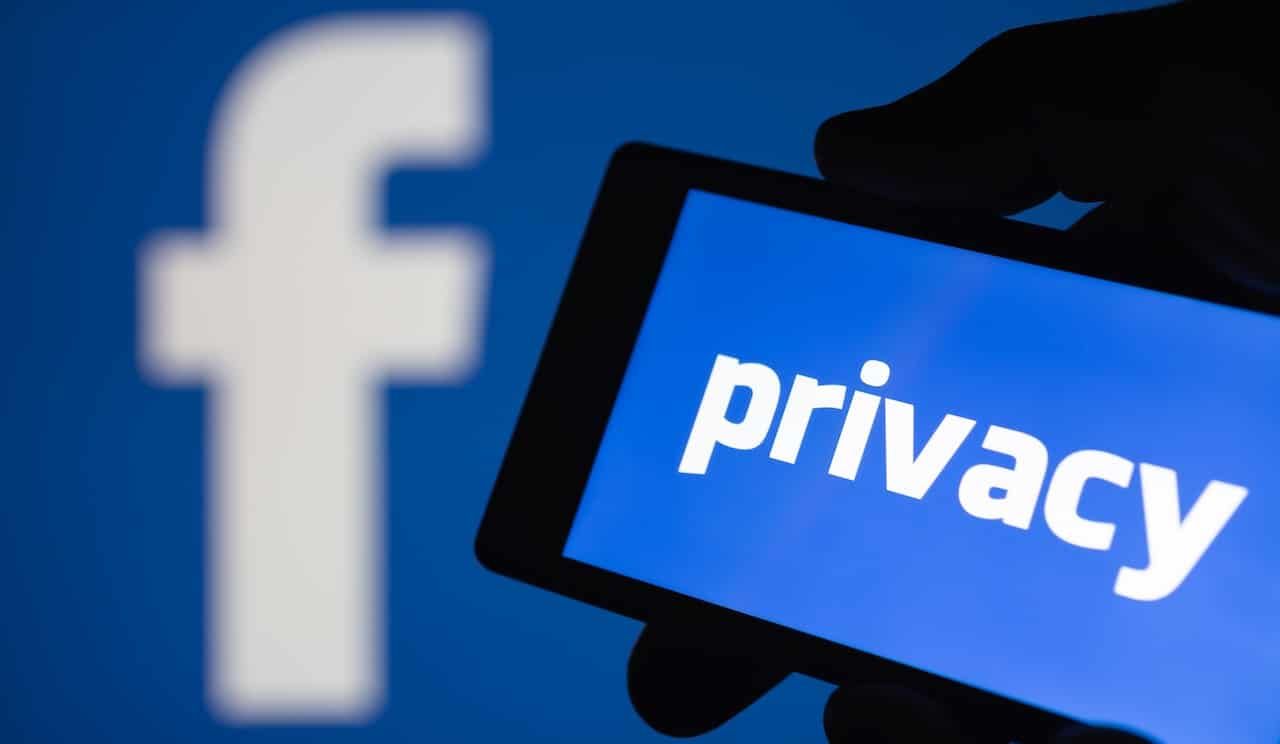 A smartphone in hand displaying the privacy text. Logo of the Facebook blurred on background.
