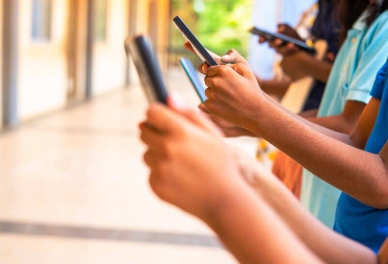Close up shot, group of children hands busy using smartphone at school corridor - concept of social media, playing games, technology and education