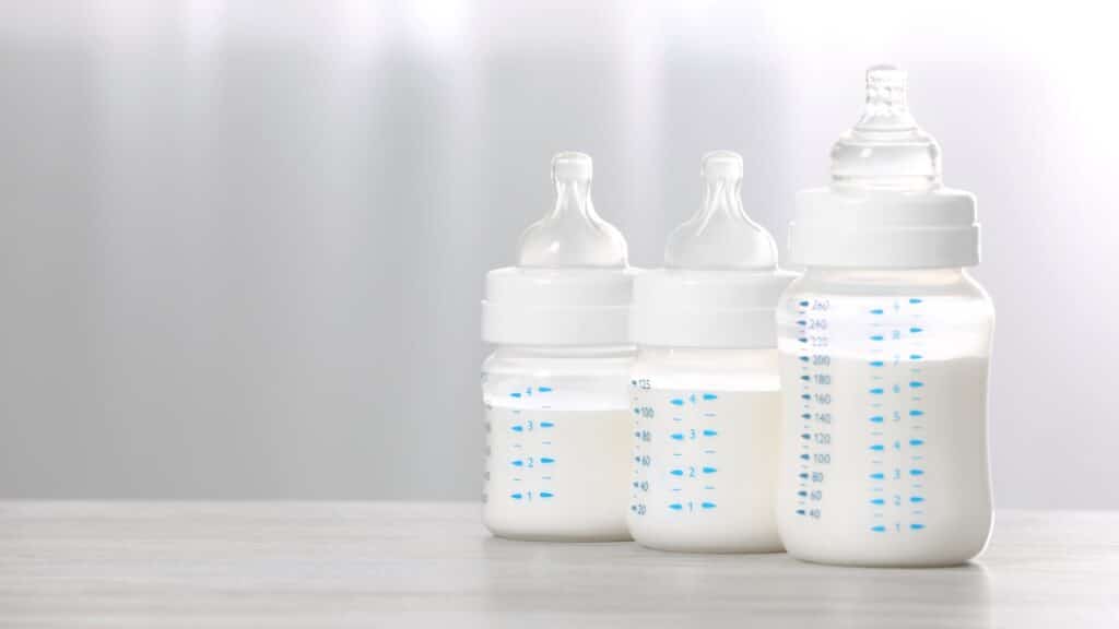 Feeding bottles with infant formula on white wooden table indoors.