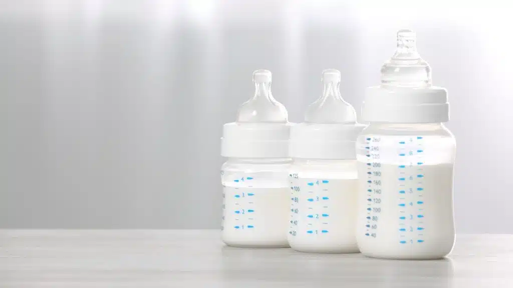 Feeding bottles with infant formula on white wooden table indoors.