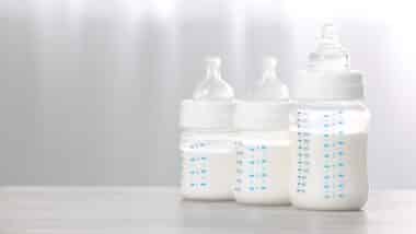 Feeding bottles with infant formula on white wooden table indoors.