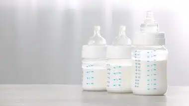 Feeding bottles with infant formula on white wooden table indoors.