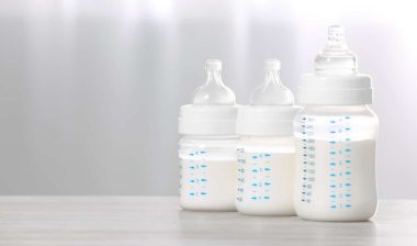 Feeding bottles with infant formula on white wooden table indoors.