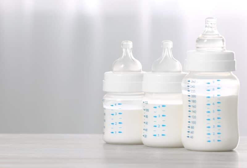 Feeding bottles with infant formula on white wooden table indoors.