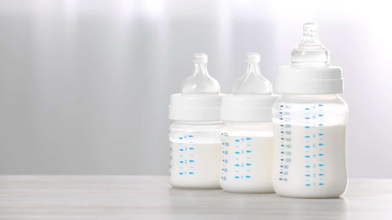 Feeding bottles with infant formula on white wooden table indoors.