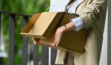 Female employee holding cardboard box full of belongings leaving office