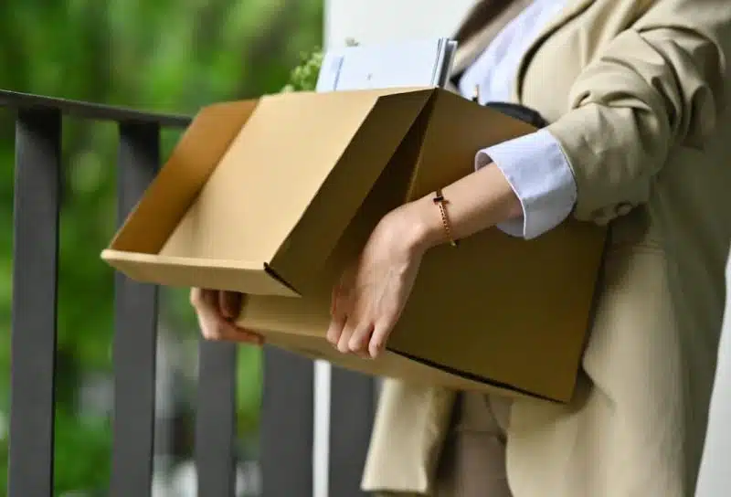 Female employee holding cardboard box full of belongings leaving office