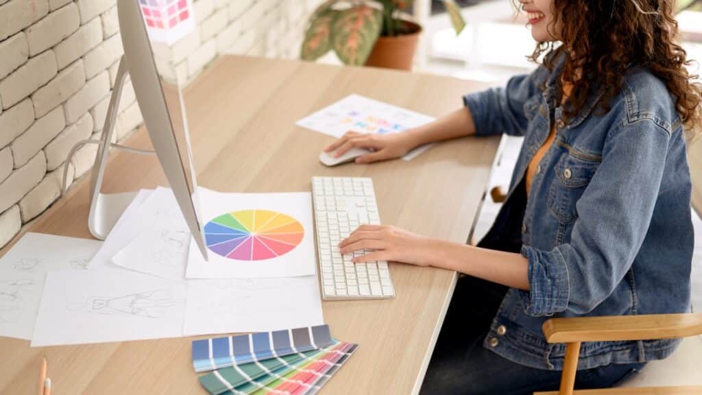Young female graphic designers sitting at desks working with computer graphics color charts and some sketches discussing the new project choosing a concept