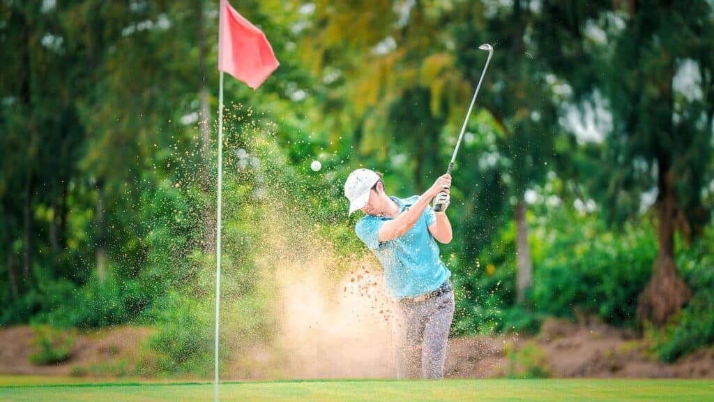 Golfer hits ball from a bunker with golf club.