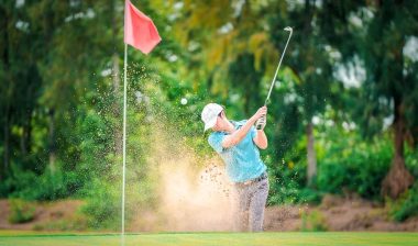 Golfer hits ball from a bunker with golf club.