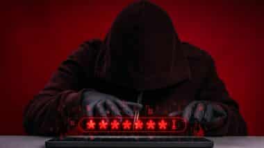 Hacker in hoodie stealing passwords by keyboard during cyberattack and data breach incident.