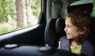 child in car seat looking out window of car