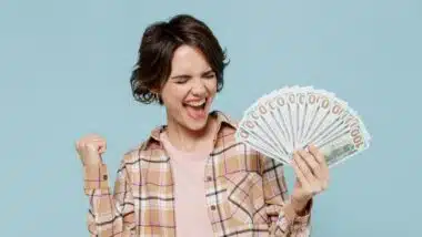 Young happy overjoyed excited woman 20s wearing casual brown shirt holding fan of cash money in dollar banknotes