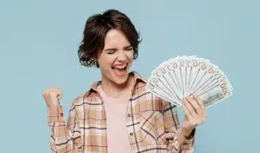 Young happy overjoyed excited woman 20s wearing casual brown shirt holding fan of cash money in dollar banknotes