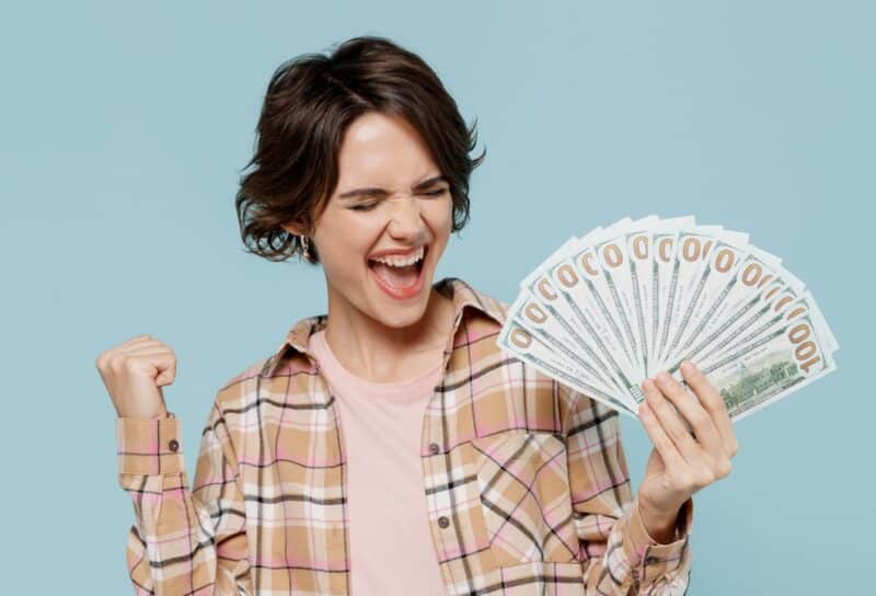 Young happy overjoyed excited woman 20s wearing casual brown shirt holding fan of cash money in dollar banknotes