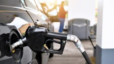 A gasoline pump handle in a gas tank of vehicle with another customer at gas pump in background