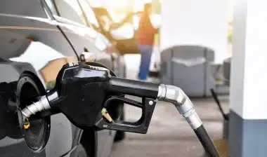 A gasoline pump handle in a gas tank of vehicle with another customer at gas pump in background