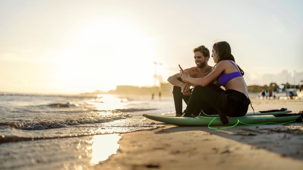 Couple is sitting on surfboards on a beach and surfing web