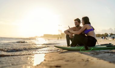 Couple is sitting on surfboards on a beach and surfing web