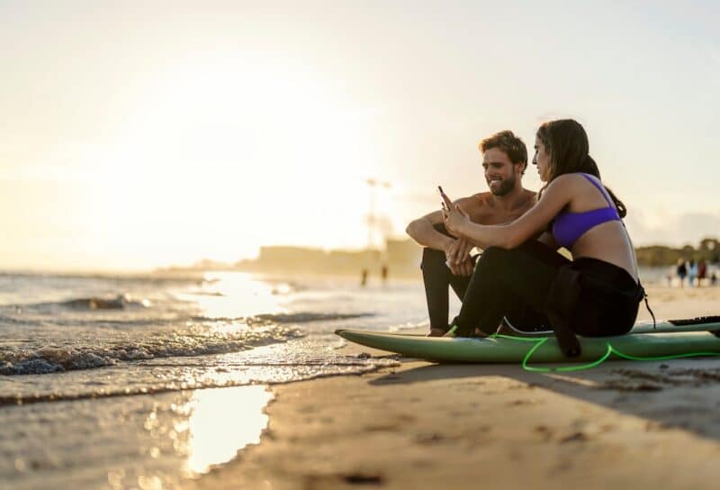 Couple is sitting on surfboards on a beach and surfing web