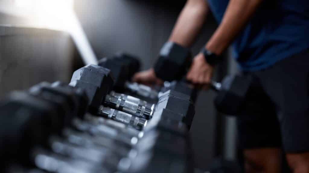 Man, hands or dumbbells in gym workout, training or exercise for strong muscle growth, healthcare wellness or bodybuilding. Zoom, texture or heavy metal weights for fitness coach or personal trainer