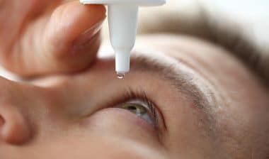 Male hand putting liquid drops in his eye