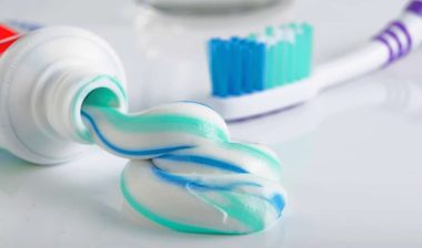 Toothbrush, tube of toothpaste and a glass on a white background