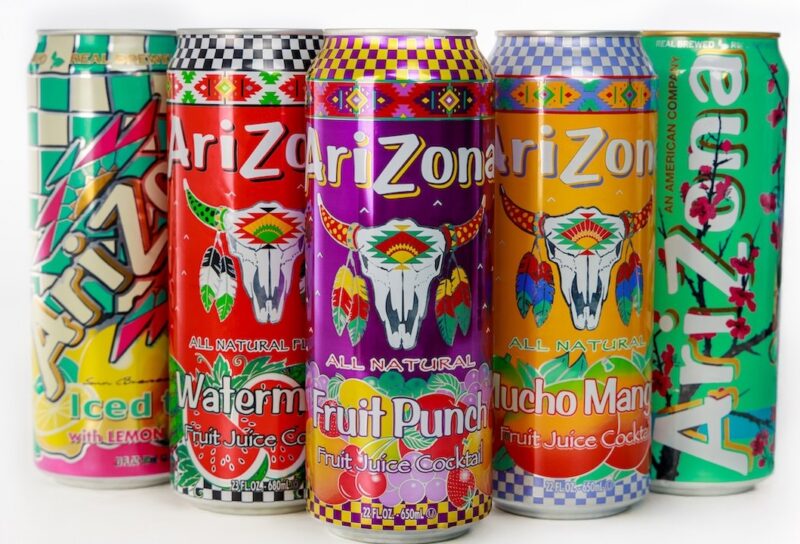 Vibrant arrangement of Arizona beverage cans featuring iced tea, watermelon, fruit punch, and much more on plain background.
