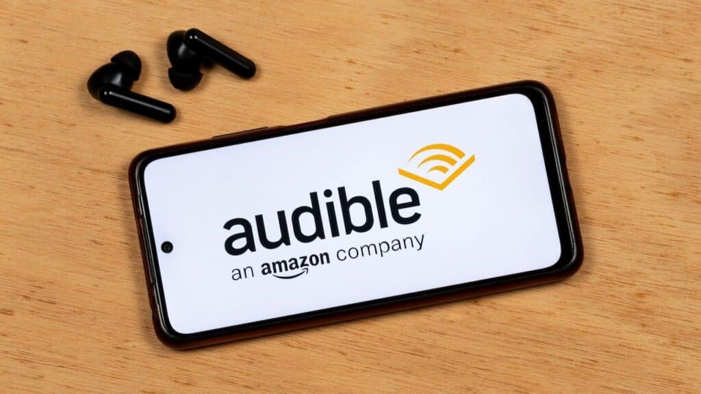 photo of a smartphone screen showing Audible app black logo with a wireless earphones over a wooden background