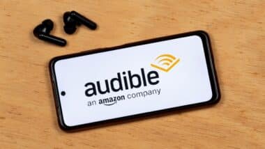photo of a smartphone screen showing Audible app black logo with a wireless earphones over a wooden background