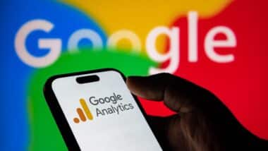 Closeup of a hand holding a smartphone displaying the google analytics logo with the google logo in the background