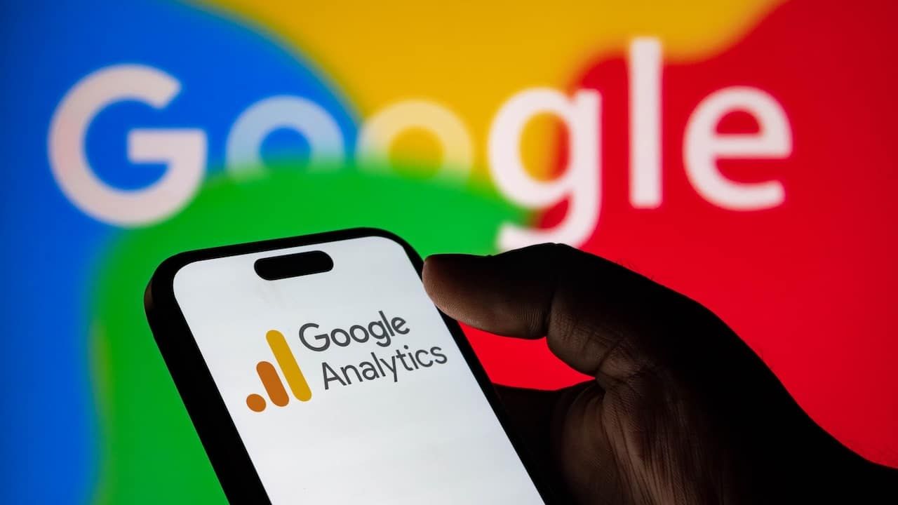 Closeup of a hand holding a smartphone displaying the google analytics logo with the google logo in the background