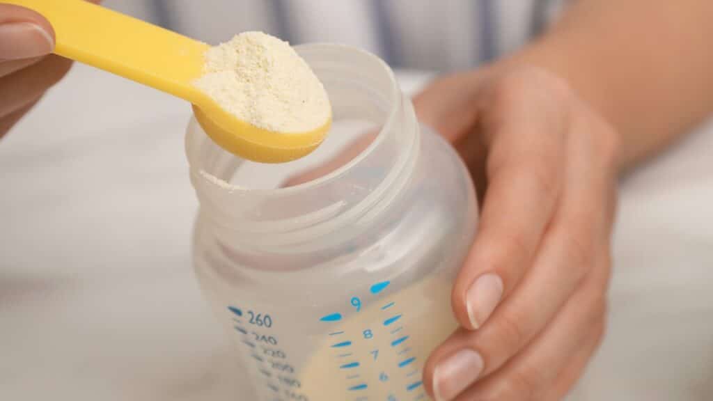Woman preparing infant formula at table, closeup. Baby milk