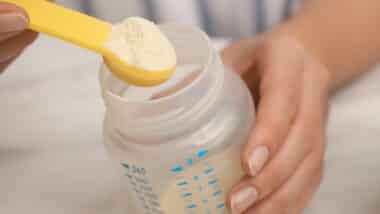 Woman preparing infant formula at table, closeup. Baby milk