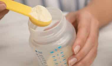 Woman preparing infant formula at table, closeup. Baby milk